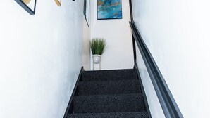 A staircase with a black carpet, a potted plant, and framed artwork on the walls. - Cosy 2bedroom House-perfect for Long & Short Stay (Wolverhampton)