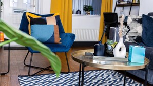 A modern living room with a blue armchair, a patterned rug, a round coffee table, and a bookshelf in the background. - Cosy 2bedroom House-perfect for Long & Short Stay (Wolverhampton)