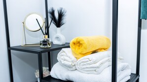 A neatly organized bathroom with a black metal shelf holding folded towels and a decorative mirror. - Cosy 2bedroom House-perfect for Long & Short Stay (Wolverhampton)