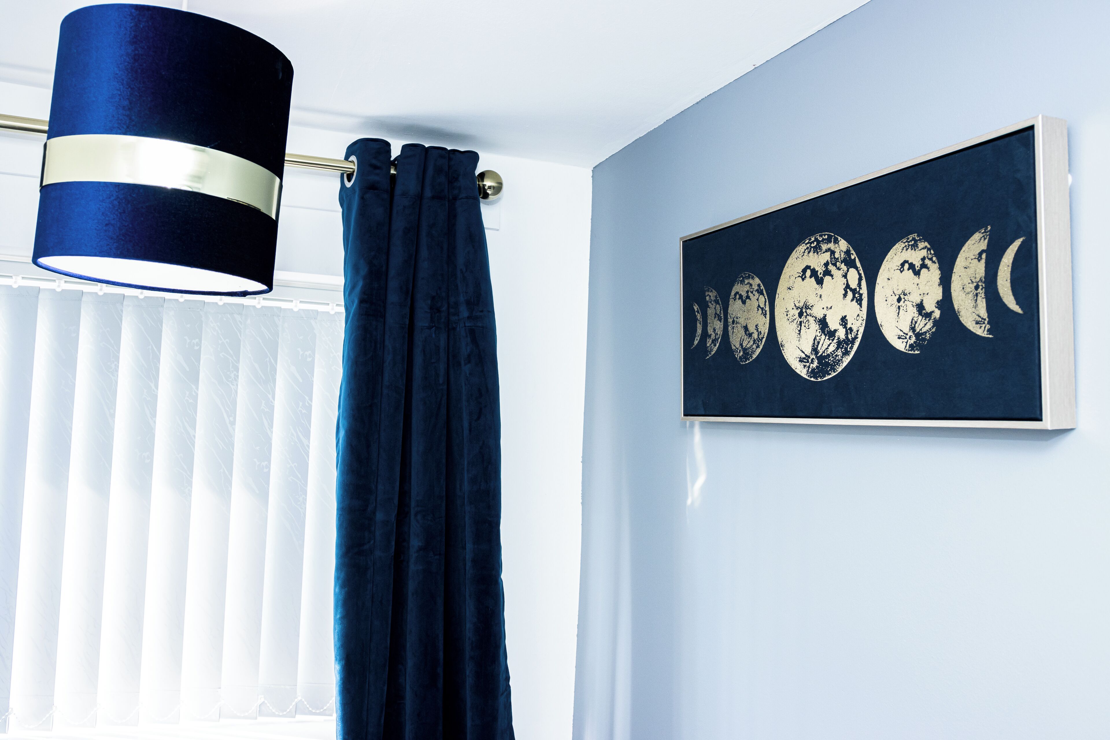 A room with a dark blue curtain, a wall-mounted lamp, and a framed moon phases artwork.