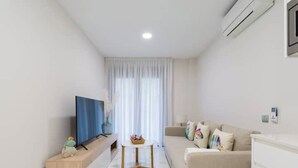 A modern living room with a flat-screen TV, a wooden side table, a beige sofa, and a marble floor. - Apartment 2 bedrooms near Las Canteras beach (Las Palmas de Gran Canaria)