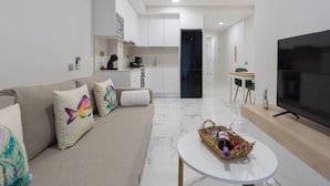 A modern living room with a sofa, a coffee table, a TV, and a kitchen area in the background. - Apartment 2 bedrooms near Las Canteras beach (Las Palmas de Gran Canaria)