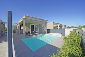 A modern outdoor pool area with a covered seating area and a clear blue pool.