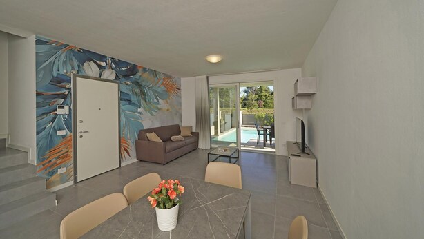 Ein modernes Wohnzimmer mit einem großen abstrakten Wandbild, einem Essbereich mit einem Marmortisch und Blick auf einen Swimmingpool durch Glastüren.