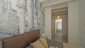 Ein Schlafzimmer mit einem großen Bett, einer Kopfteil und Wandmalerei. Eine Tür führt in einen weiteren Raum.