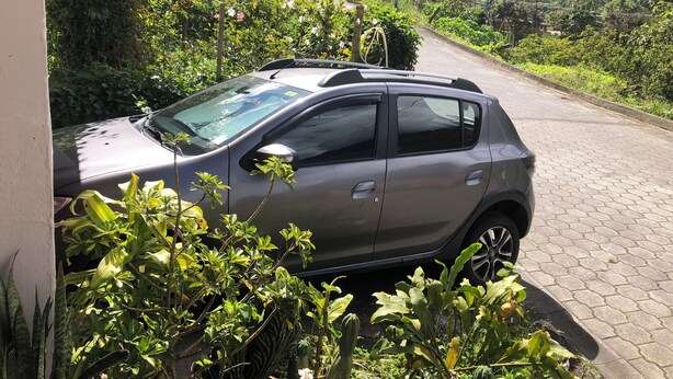 A parked car in a lush, green area with a paved path and a fence. -  Athene Moon, ubicados en el barrio "San Vicente" diagonal a Refugio Spa (Baños de Agua Santa)
