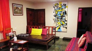 A room with a bed, a wooden chair, a small table with a bottle and remote control, and a colorful artwork on the wall. -  Athene Moon, ubicados en el barrio "San Vicente" diagonal a Refugio Spa (Baños de Agua Santa)