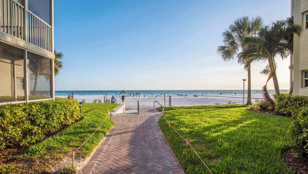 A pathway leading to a beach with a clear view of the ocean, surrounded by greenery and palm trees.
