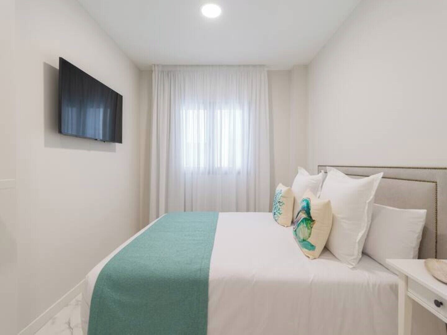 A hotel room with a bed, a TV mounted on the wall, and a window with curtains.