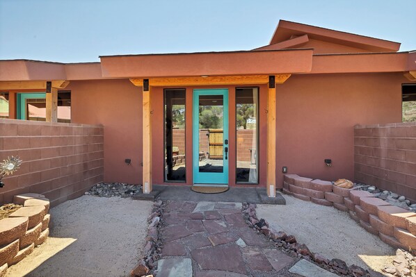 Un bâtiment moderne doté d’une porte turquoise remarquable, d’un chemin de pierre menant à l’entrée et d’un mur de briques qui entoure la propriété.