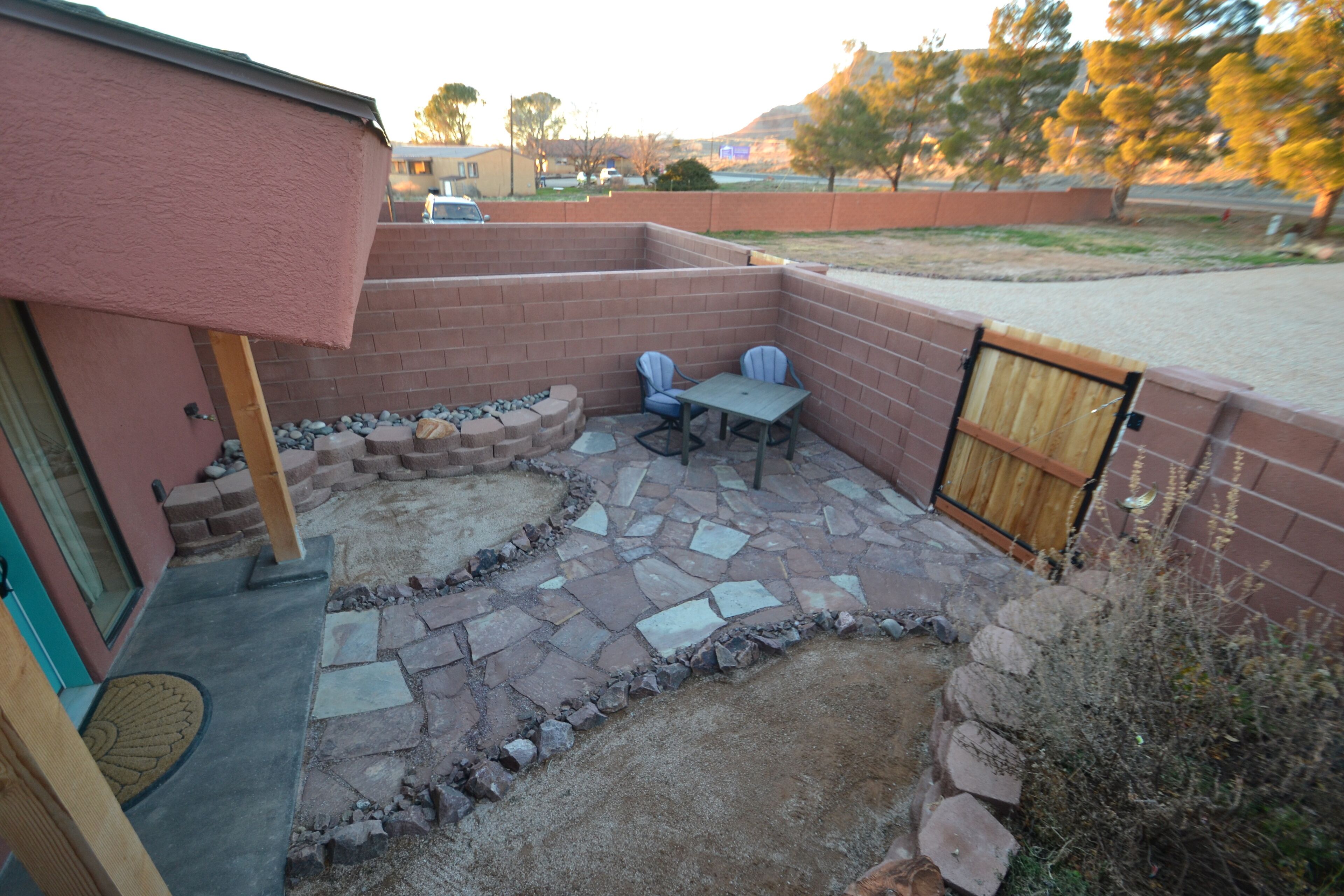 A patio area with a brick wall, a stone-tiled floor, and a wooden table with two chairs.