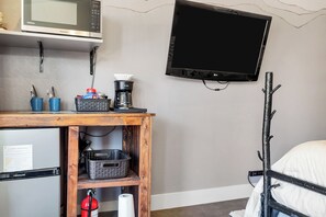 Une chambre de taille modeste équipée d’un lit, d’un téléviseur fixé au mur, d’un four à micro-ondes, d’une machine à café et d’un réfrigérateur.