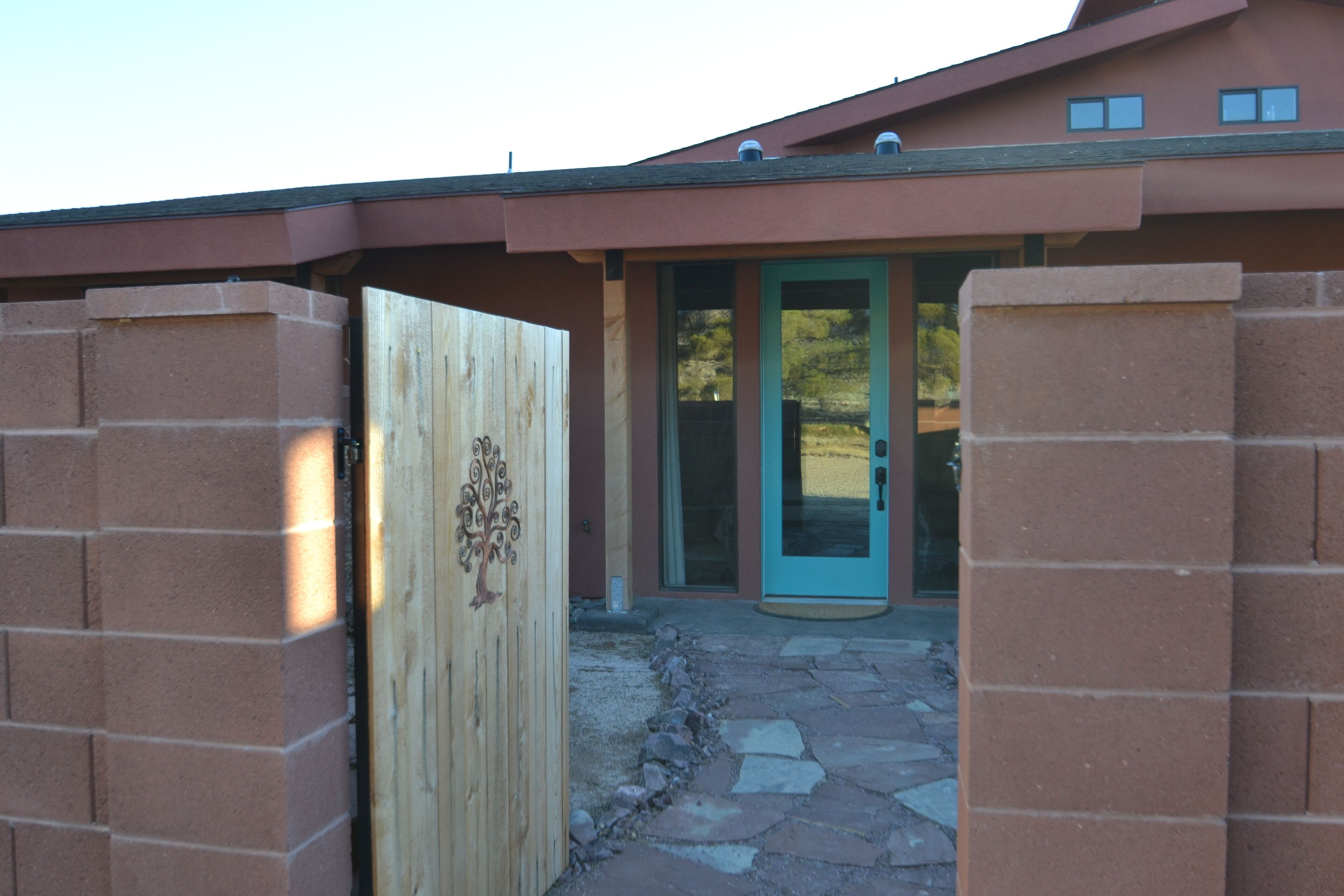 A building entrance with a wooden gate, a blue door, and a stone pathway leading to a glass door.