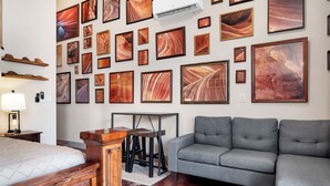 Une pièce comprenant un lit, un canapé gris, une armoire en bois et un mur décoré d’œuvres d’art encadrées.