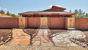 Une maison moderne avec une façade en briques, un portail en bois et un chemin de pierre menant à l’entrée.