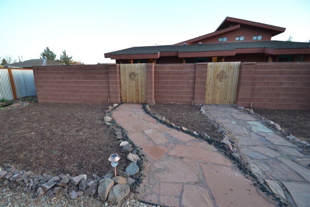 A brick wall with a wooden gate, a stone pathway, and a building with a red roof.