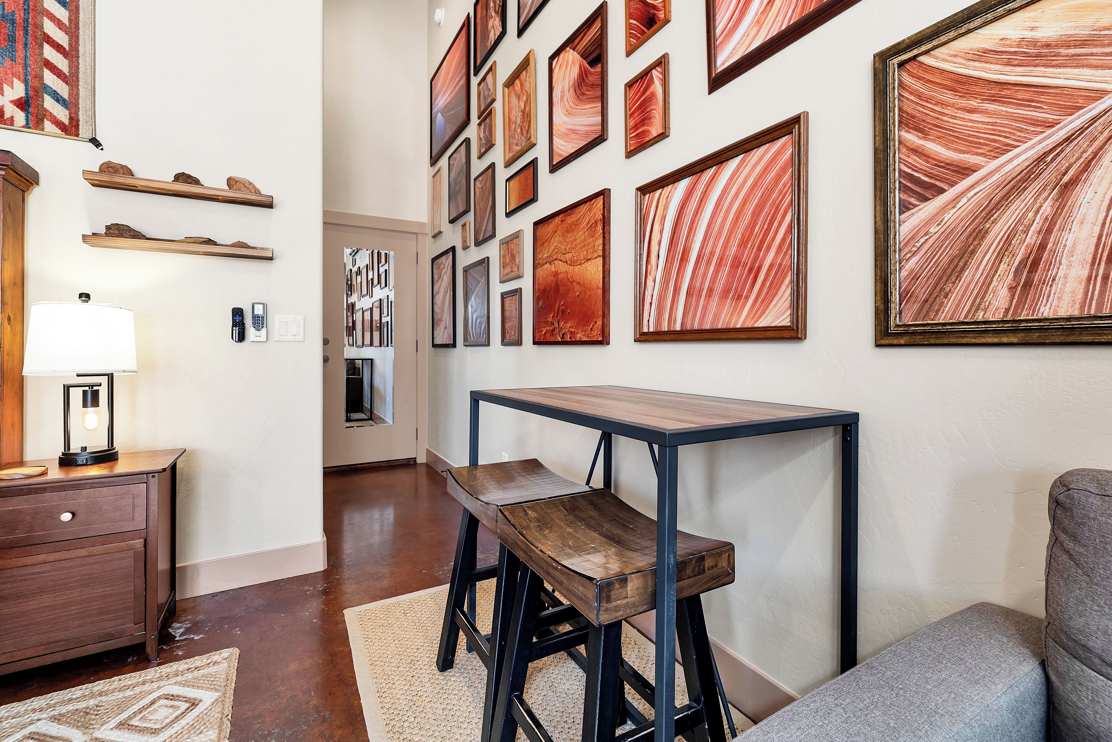 A room with a wooden desk, a chair, a lamp, and a wall adorned with framed artwork.