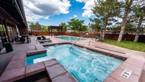 Piscina rectangular con hidromasaje, rodeada por una terraza de madera y sillas de descanso.