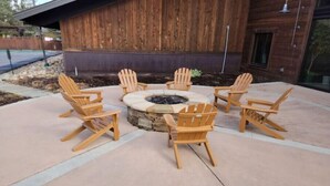 Un espacio al aire libre con asientos circulares, seis sillas Adirondack alrededor de un hogar a leña de piedra.