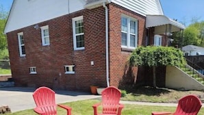 Una casa de ladrillo con techo blanco y un pequeño hogar rodeado de sillas Adirondack rojas.