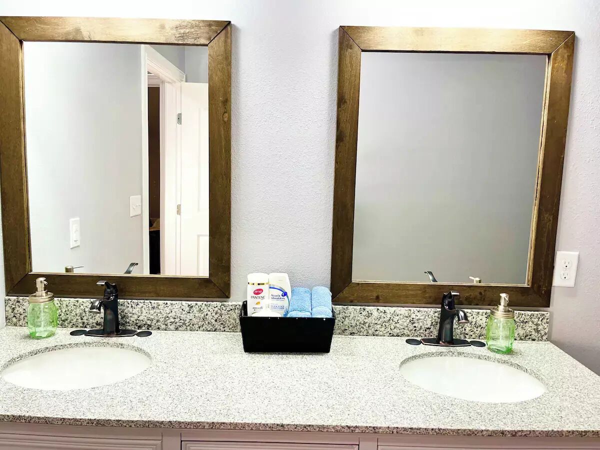 A bathroom with two sinks, a mirror, and a black basket containing toiletries.