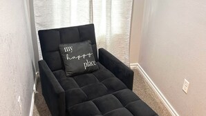 A black sofa with a cushion that reads 'my happy place' in a corner of a room with a carpeted floor and a window with sheer curtains. - My house your house (Fort Smith)