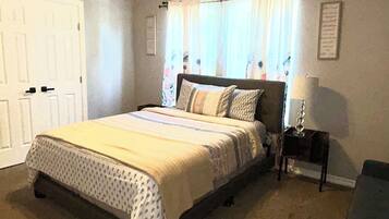 Une chambre à coucher avec un lit, un ventilateur de plafond, une table de chevet, une lampe et une fenêtre avec des rideaux.