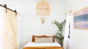 Un dormitorio con una cama, una lámpara de pared, una planta y un cuadro.