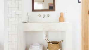 Un baño con lavamanos de mármol blanco, una puerta de madera y una cesta tejida debajo del lavamanos.