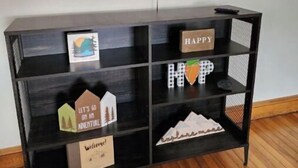 Un meuble noir pour téléviseur, doté d’étagères, avec un téléviseur à écran plat fixé au-dessus, et un plancher en bois.