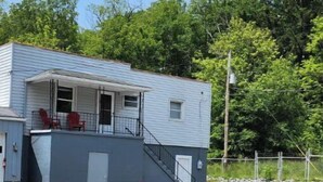 Un bâtiment à deux étages doté d’un porche couvert et d’un petit espace extérieur aménagé avec quatre chaises Adirondack rouges.