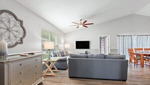 A modern living room with a grey sofa, wooden dining table, and a ceiling fan. - Disney themed house with heated private pool. 15 minutes from Disney (Davenport)