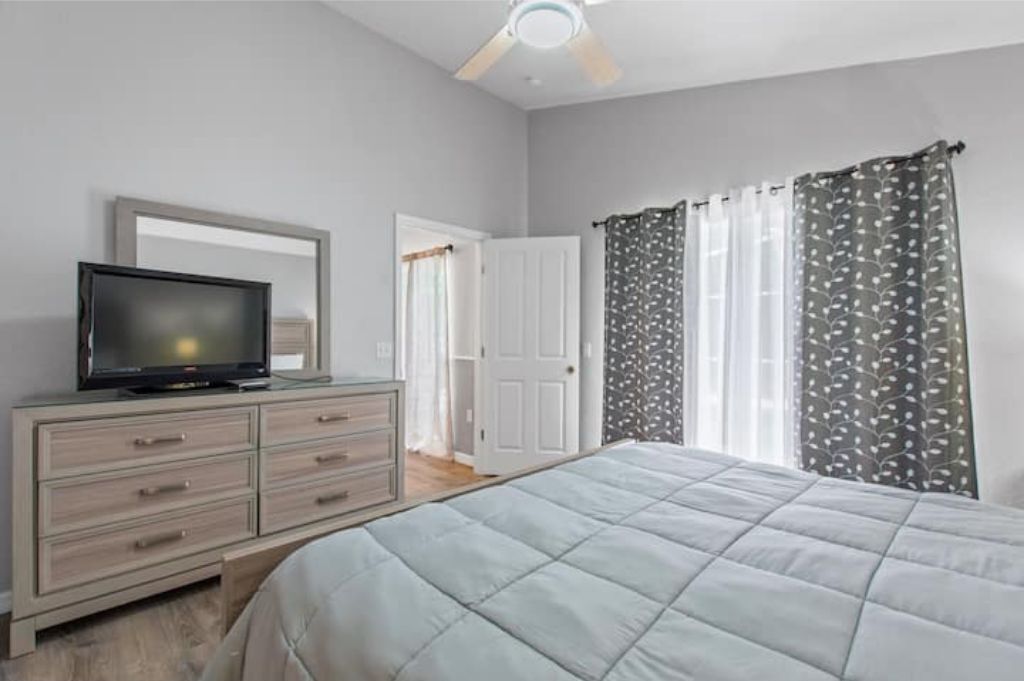 A bedroom with a bed, a dresser, a television, and a door leading to another room.