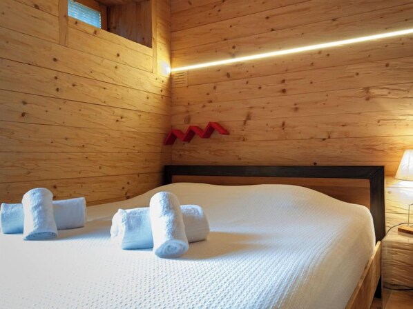 A wooden cabin room with a bed, towels, and a nightstand.
