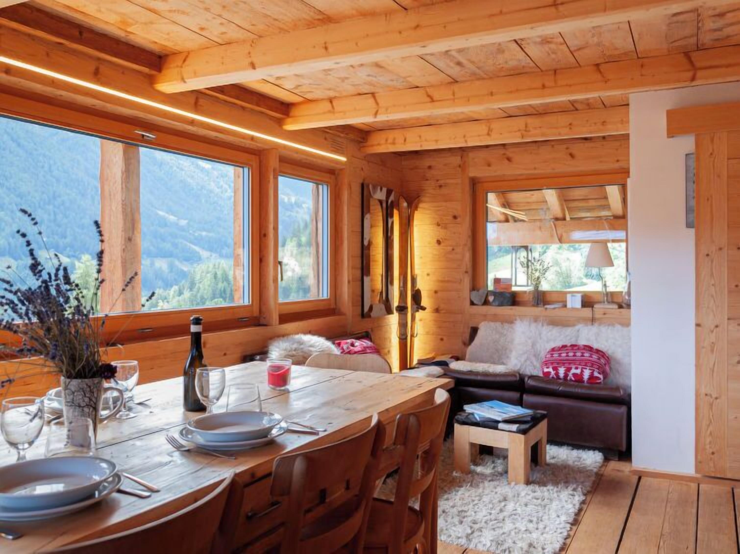 Een houten cabin met een eethoek, een bank en uitzicht op de bergen.