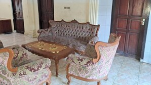 Una habitación con un sofá grande y ornamentado, sillones a juego, una mesa de centro de madera y dos puertas.