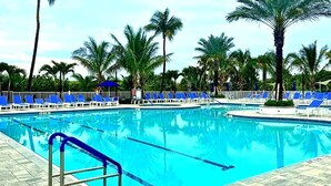 A swimming pool with blue chairs and palm trees. - Private Beach Resort Condo, Hutchinson Island, FL (Fort Pierce)