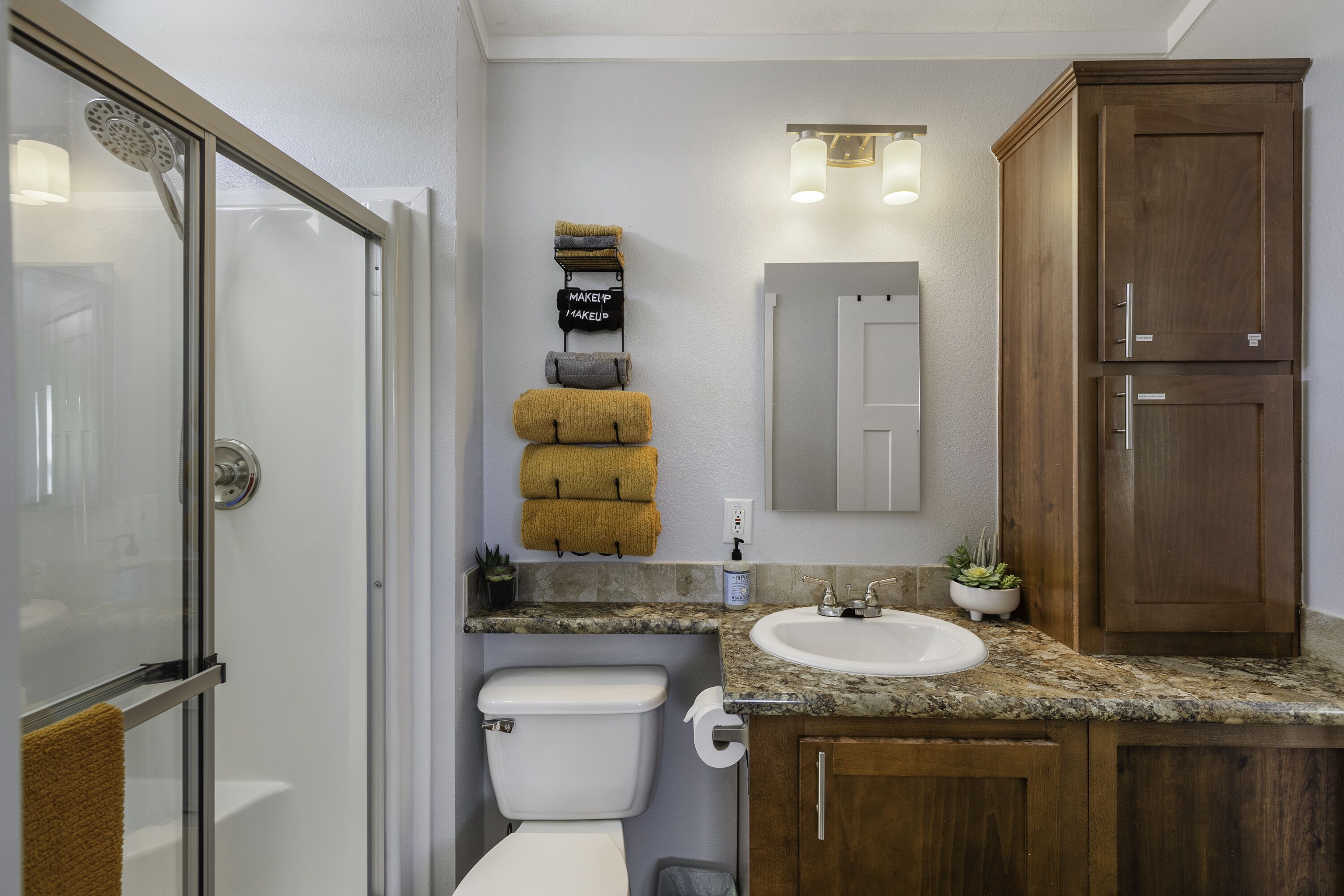 Ein Badezimmer mit Glasdusche, Toilette, Waschbecken und Holzschränken.