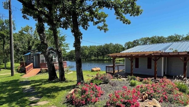 Ein Seehaus mit einer Terrasse, umgeben von einem Garten mit rosa Blumen und einem Steinweg.
