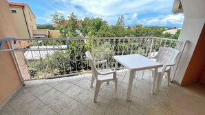 A balcony with a white table and chairs, a metal railing, and a view of buildings and trees.