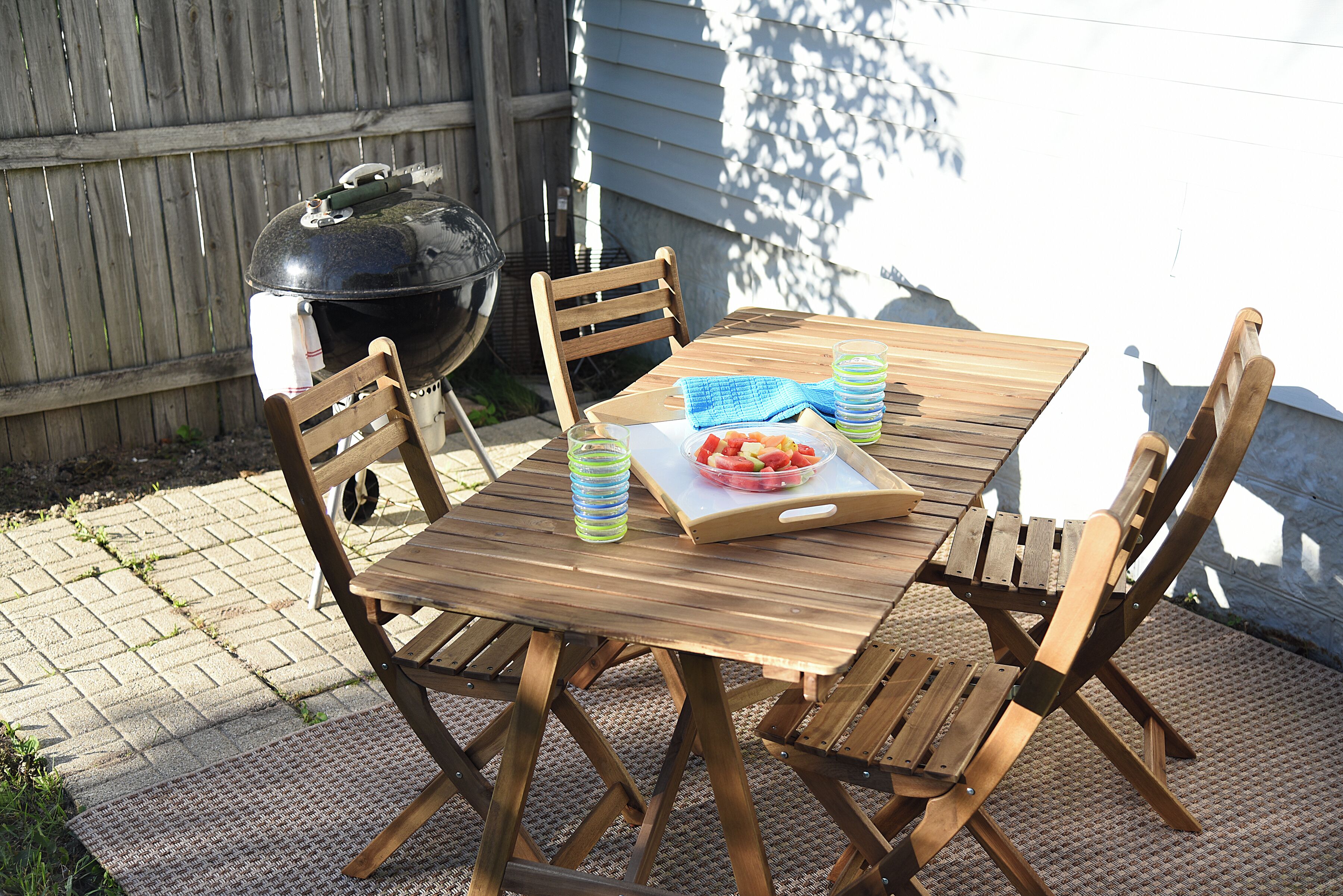 A wooden table with chairs, a grill, and a tray with food and drinks.