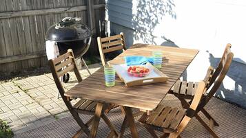 A wooden table with chairs, a grill, and a tray with food and drinks.