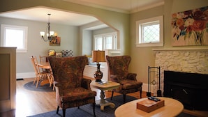 A living room with a fireplace, two patterned armchairs, a dining table with chairs, and a chandelier. - House in Quaint Neighborhood near Downtown Milwaukee Pet-Friendly! (Milwaukee)