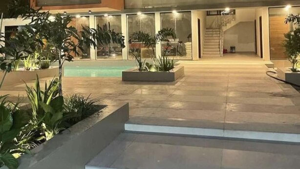 A modern multi-story house with a pool, outdoor lighting, and a staircase leading to the upper levels. - Modern Nearby Beach Apartment (Serrekunda)