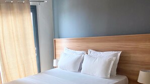 A modern hotel room with a large bed, wooden headboard, white bedding, and a bedside table with a lamp. - Modern Nearby Beach Apartment (Serrekunda)