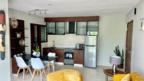 A modern kitchen with a built-in oven, a refrigerator, and a dining area with a table and chairs. - Modern Nearby Beach Apartment (Serrekunda)