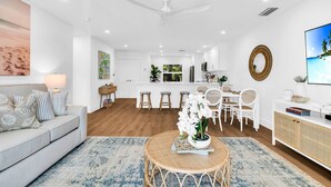A modern living room with a sofa, a round table with a plant, and a dining area with white chairs. - ON The Beach Juno! 4-Steps to the Beach! (Juno Beach)