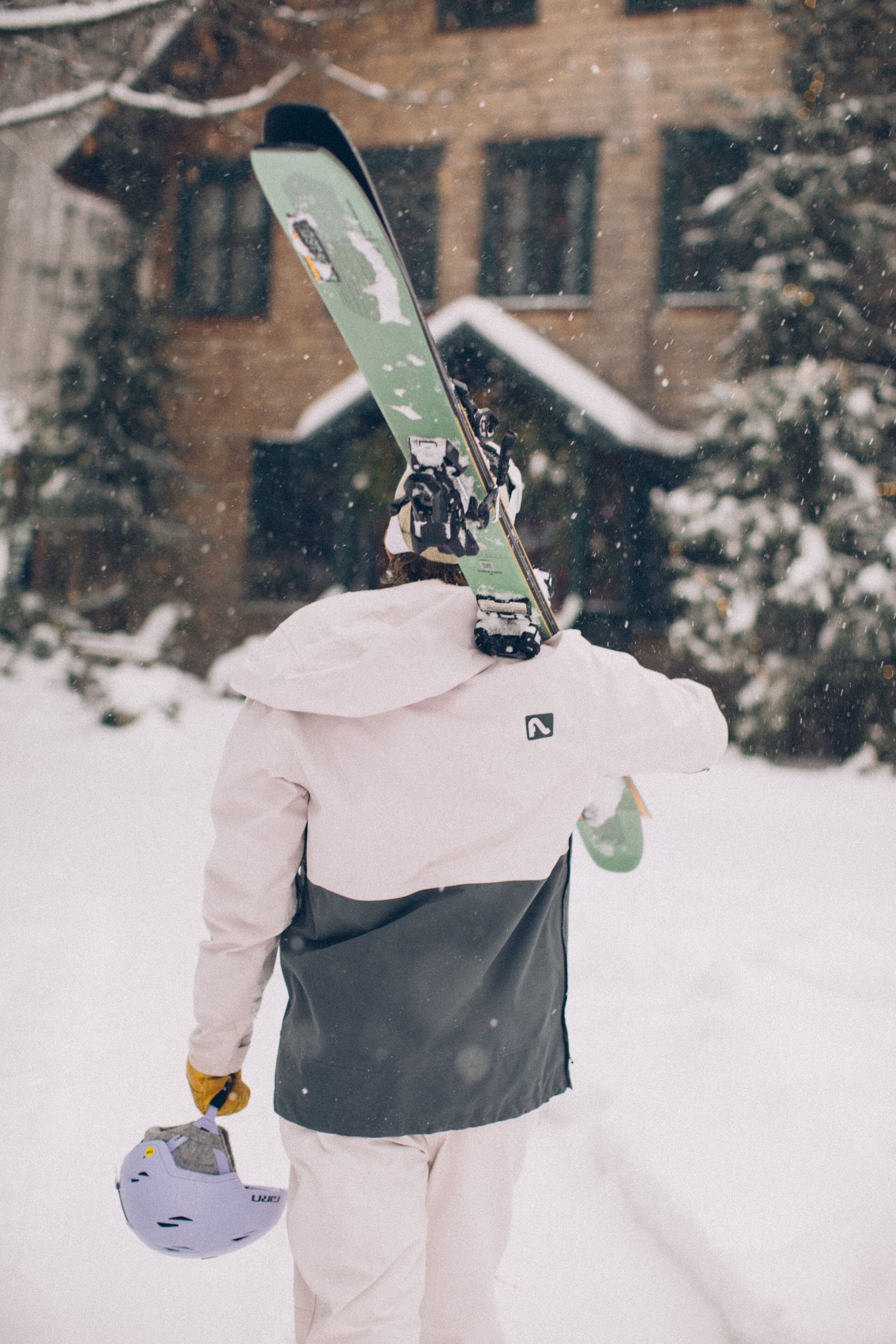 A person wearing a white and black jacket, holding a snowboard and helmet.