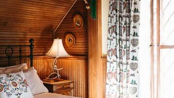A wooden-paneled room with a bed, a nightstand, a lamp, and a window with patterned curtains.