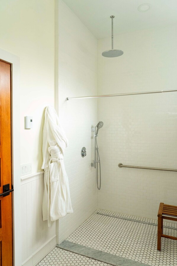A shower area with a white tiled wall, a handheld showerhead, a towel rack with a white towel, and a wooden bench. - Deer Mountain Inn (Haines Falls)